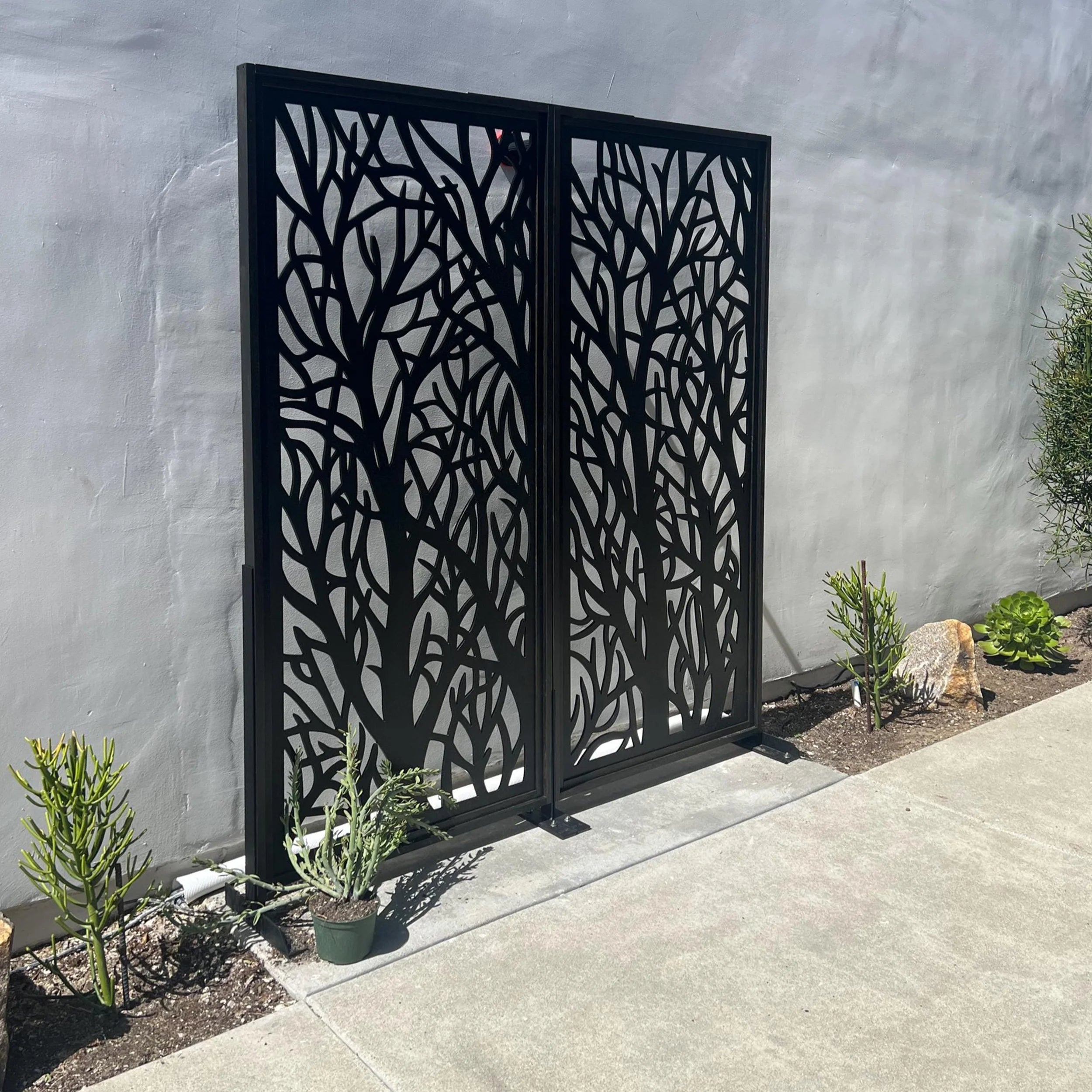 Decorative black metal screen with tree branch design against a gray wall.