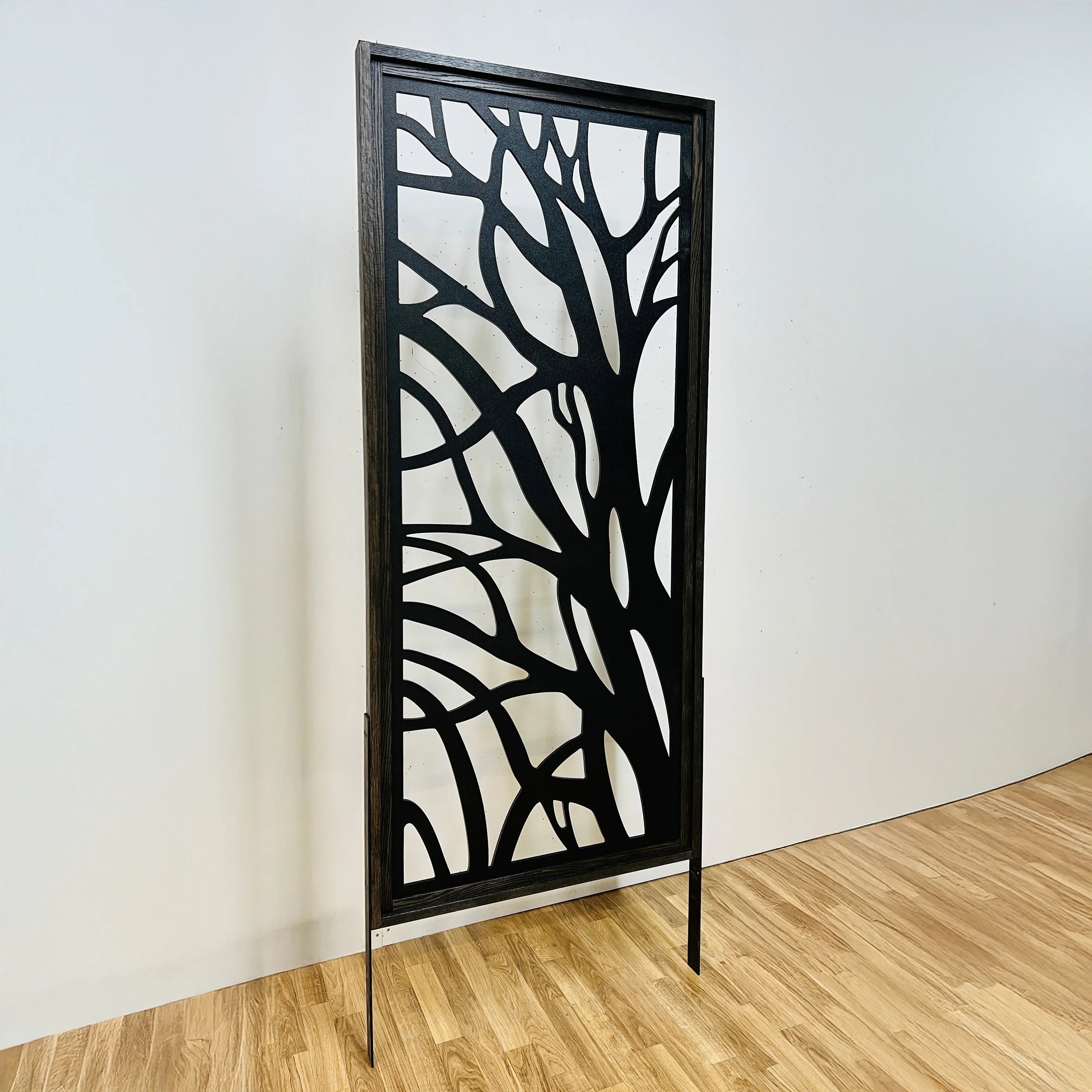 Decorative metal screen with tree branch design on a wooden floor against a white wall.