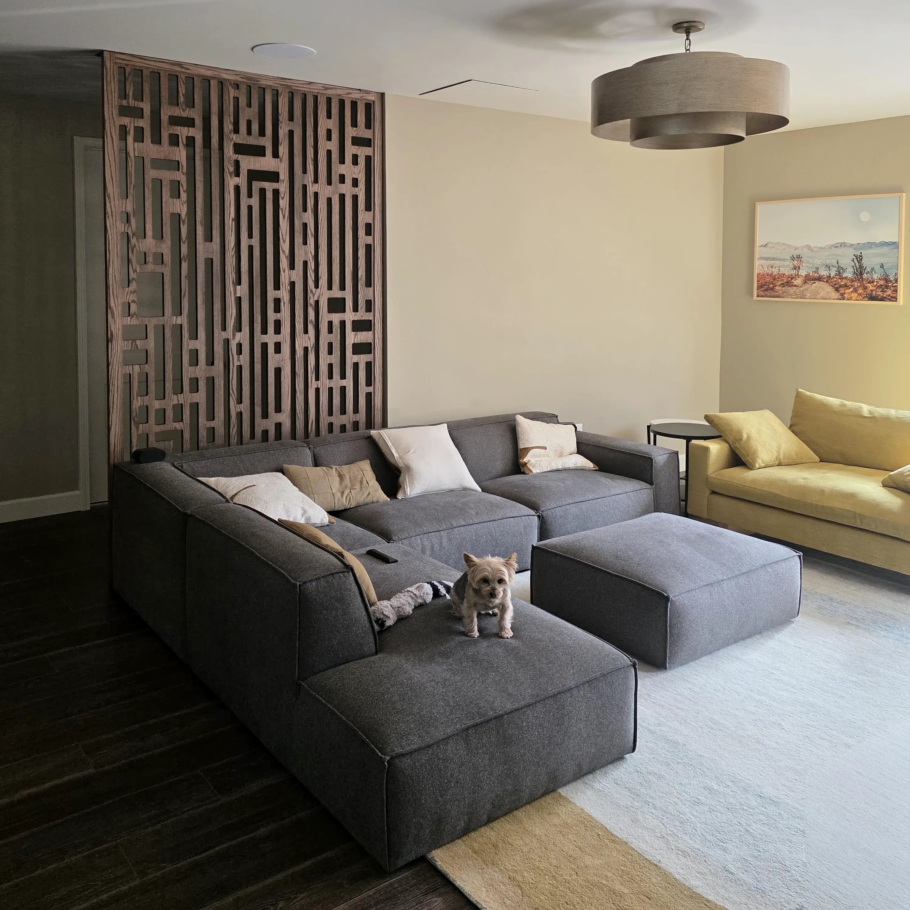 Modern living room with a gray sectional sofa, yellow armchair, and decorative wall art.
