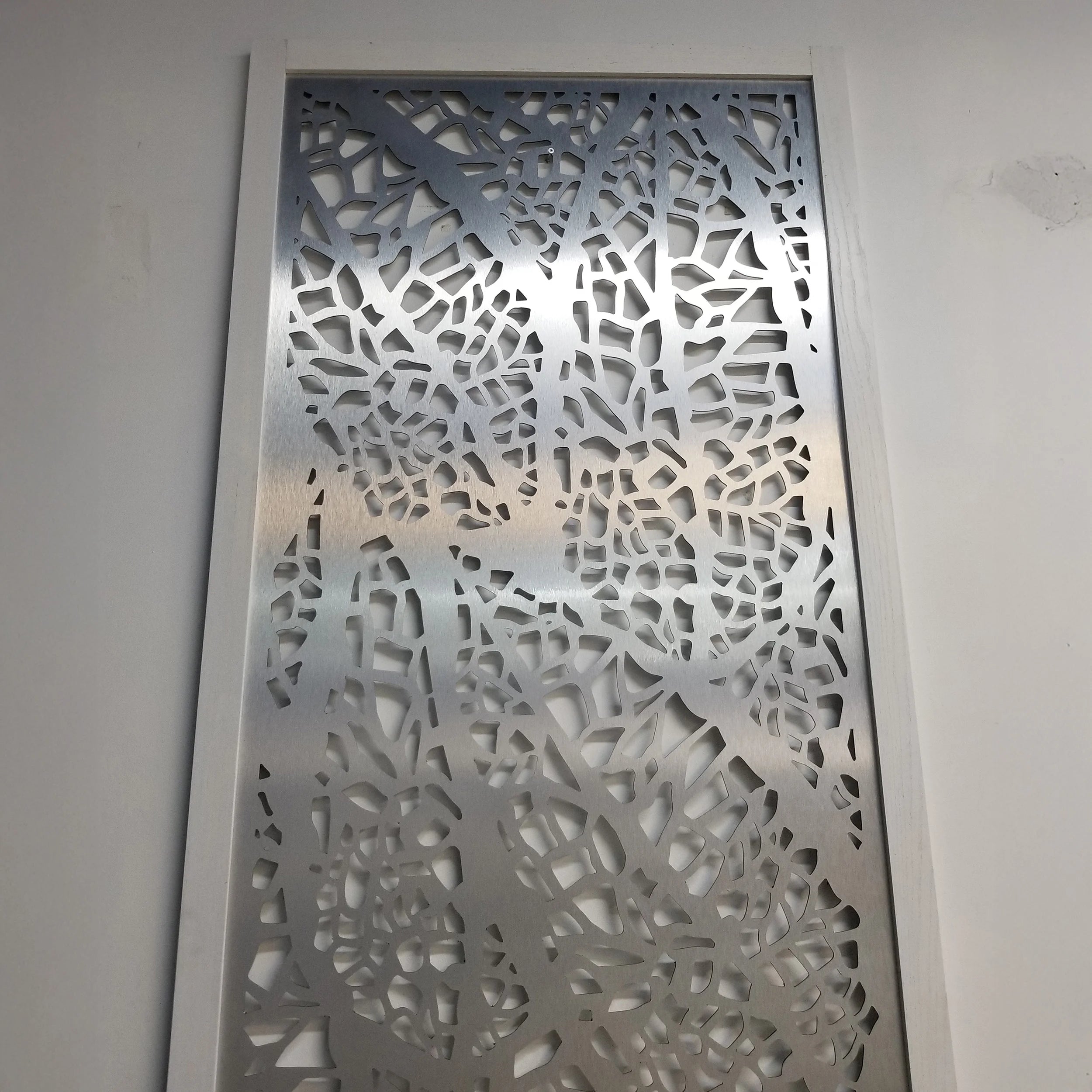 Decorative metal panel with intricate cut-out design on a white wall