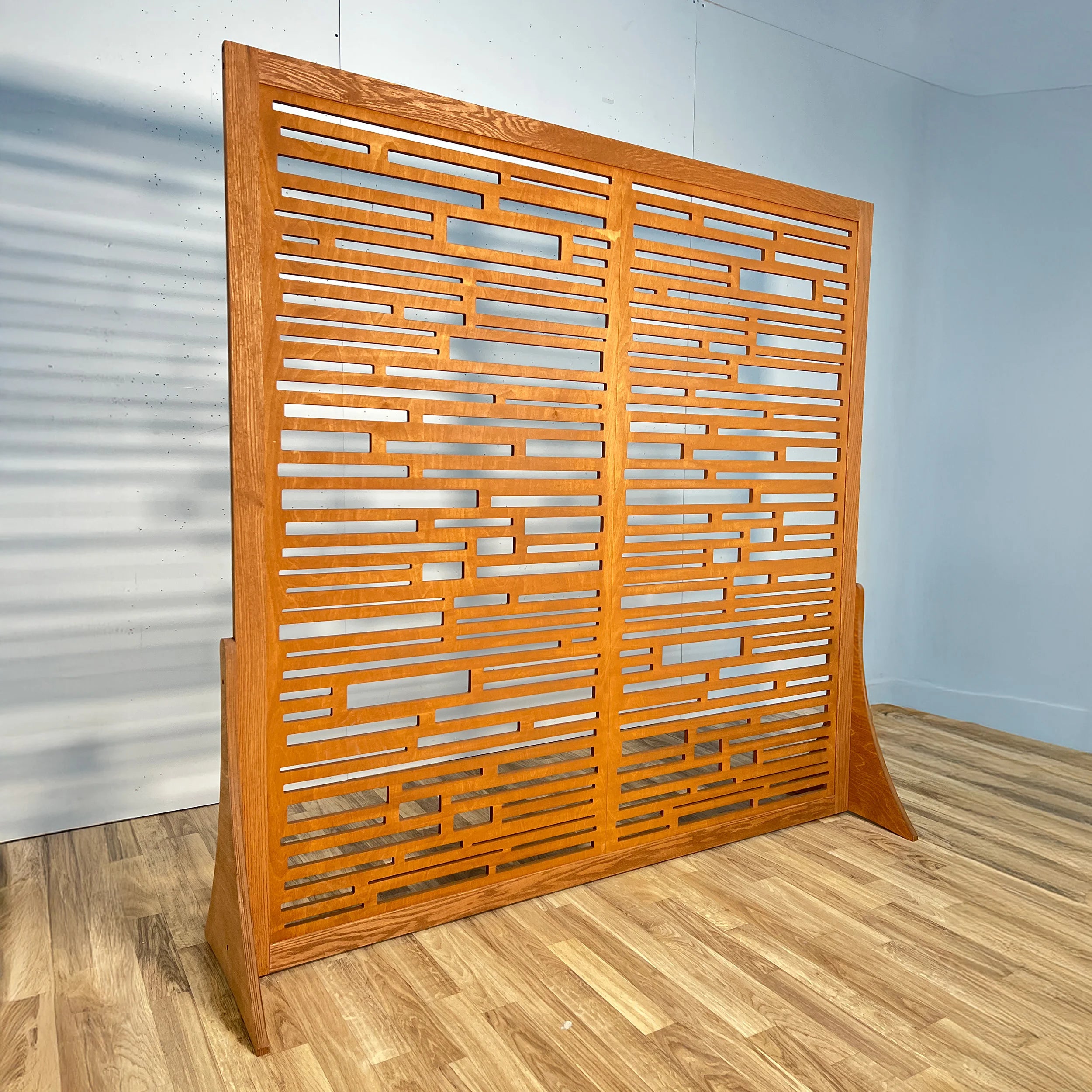 Wooden room divider with geometric pattern on a wooden floor and light blue wall background