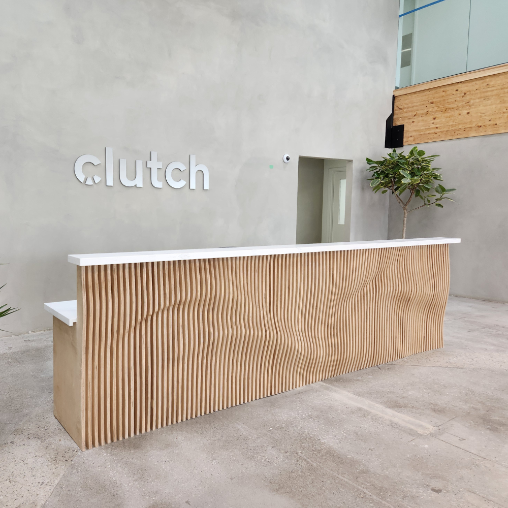 Wooden reception desk with 'Clutch' logo on a concrete wall