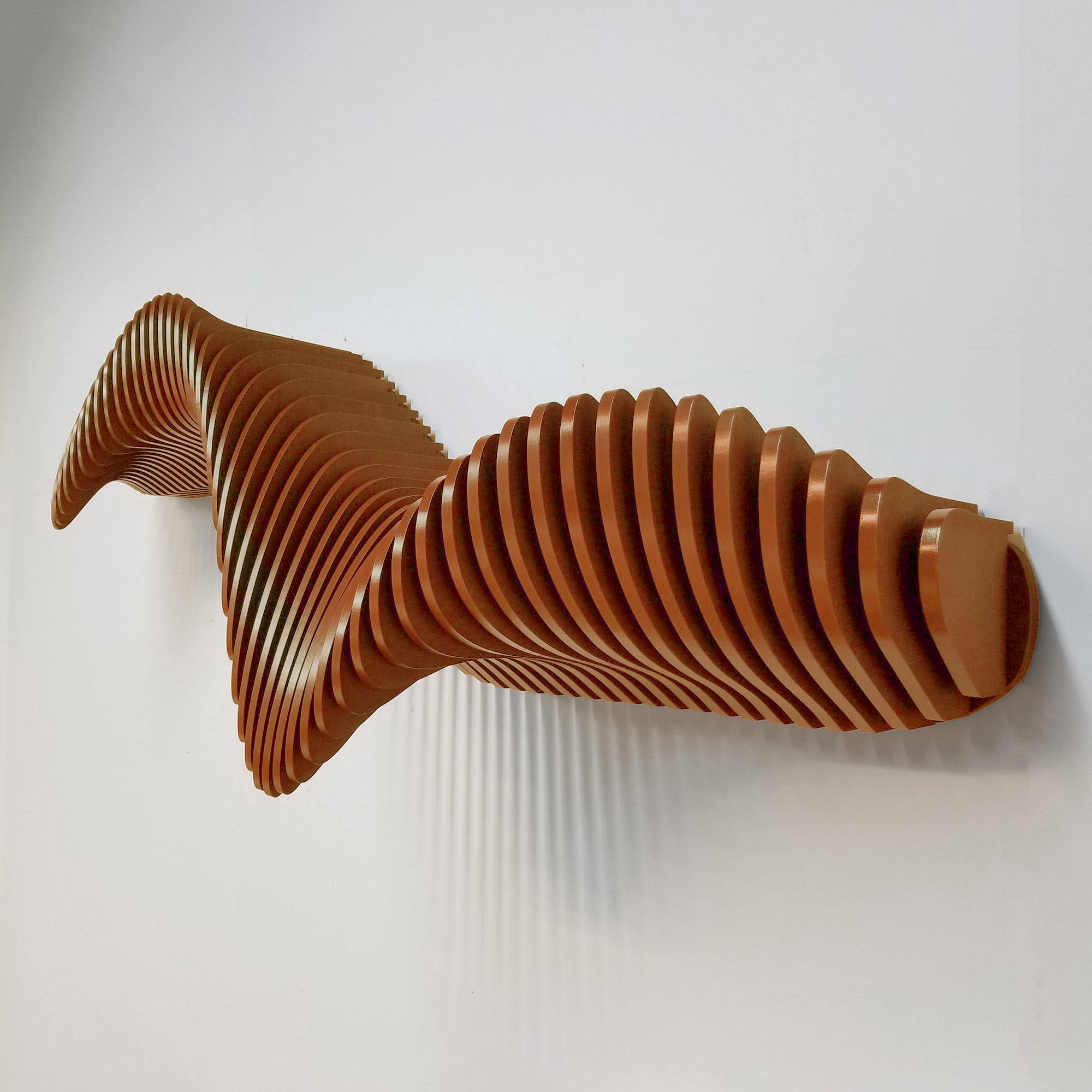 A wall-mounted, curved brown shelf with a smooth, glossy finish mounted on a green wall in an interior setting. The shelf is positioned above a white console table with a vase containing dried flowers.