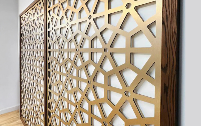 Decorative metallic screen with geometric pattern on a white wall.