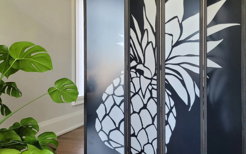 Decorative glass panel with white floral design on a black background, next to a green plant.