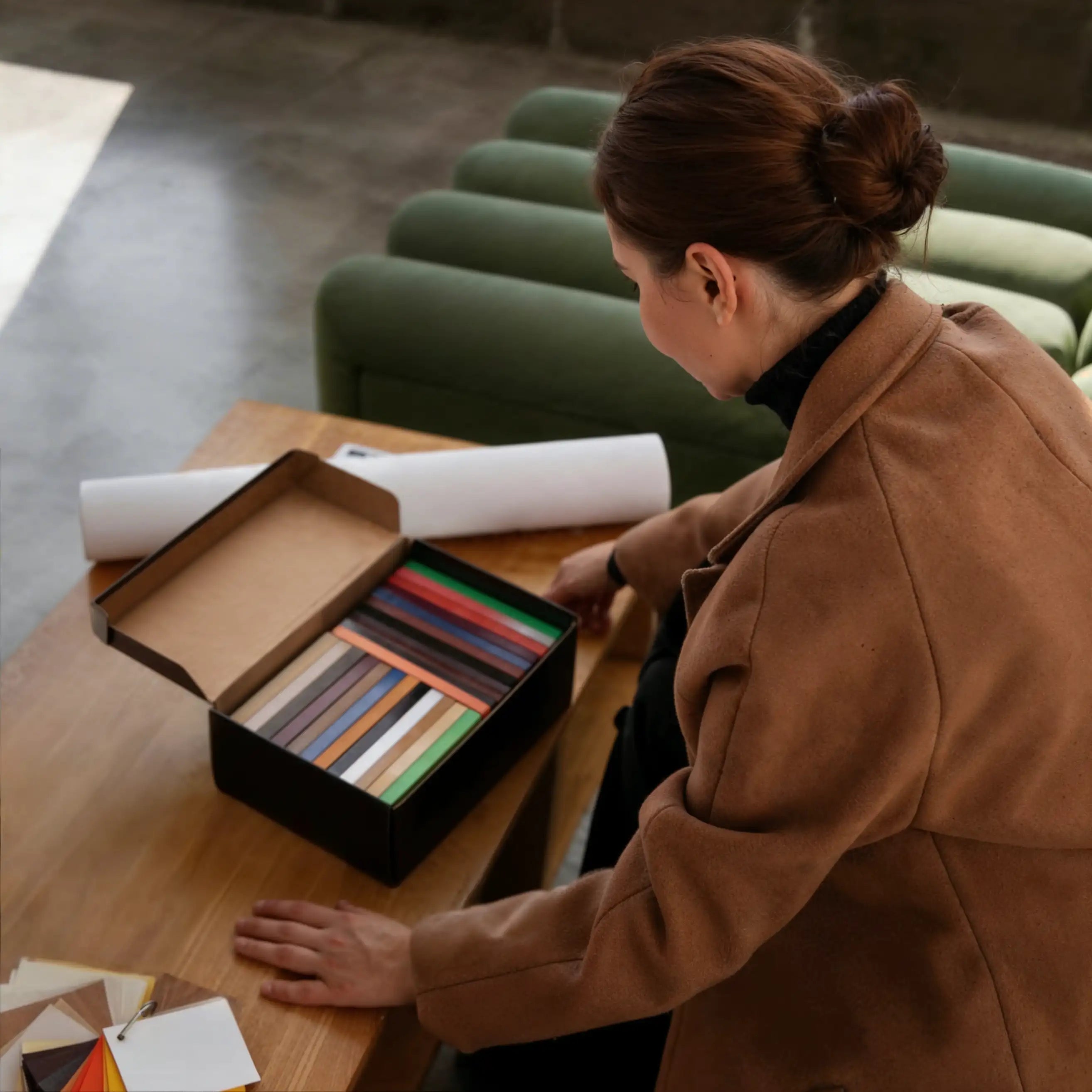 Woman in a brown coat looking at color swatches on a wooden table.