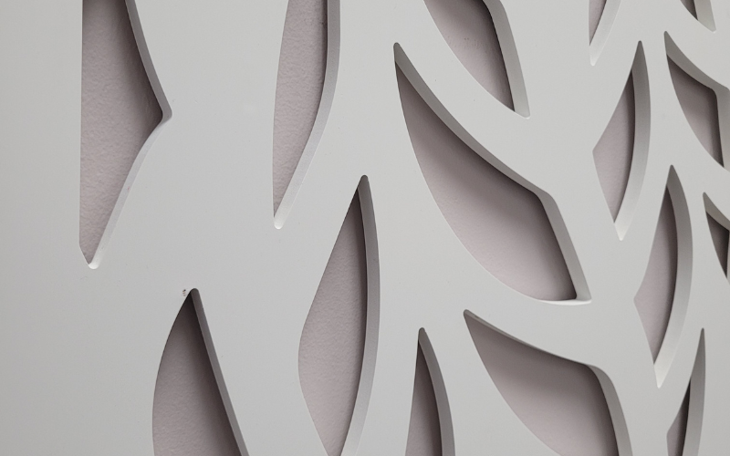 Close-up of a decorative wall panel with geometric cut-out patterns on a light gray background.